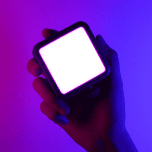 Hand holding Ulanzi VL49 portable mini RGB light emitting bright white light with purple-blue ambient RGB glow showing palm-sized compact design