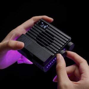 Ulanzi LE20 held in two hands showing OLED display screen, control knobs, and purple RGB glow from LED panel on dark background
